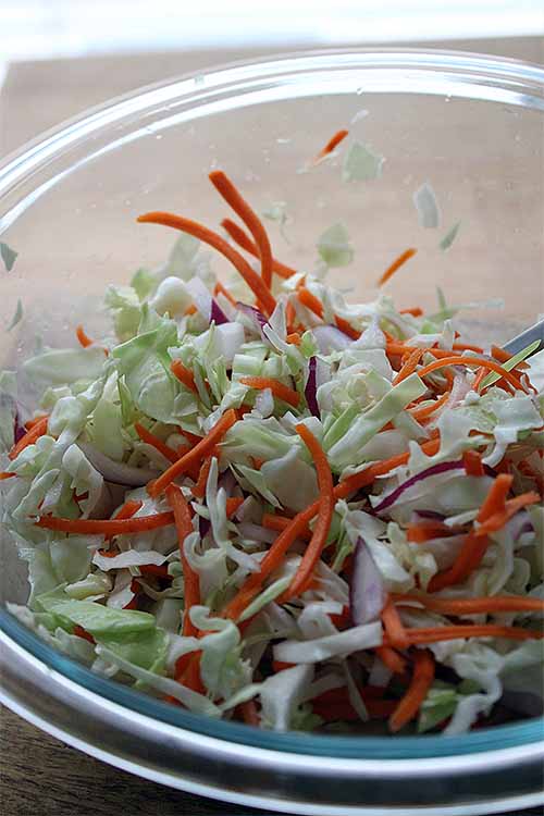 Closely cropped image of a clear glass bowl of shredded cabbage and carrots.