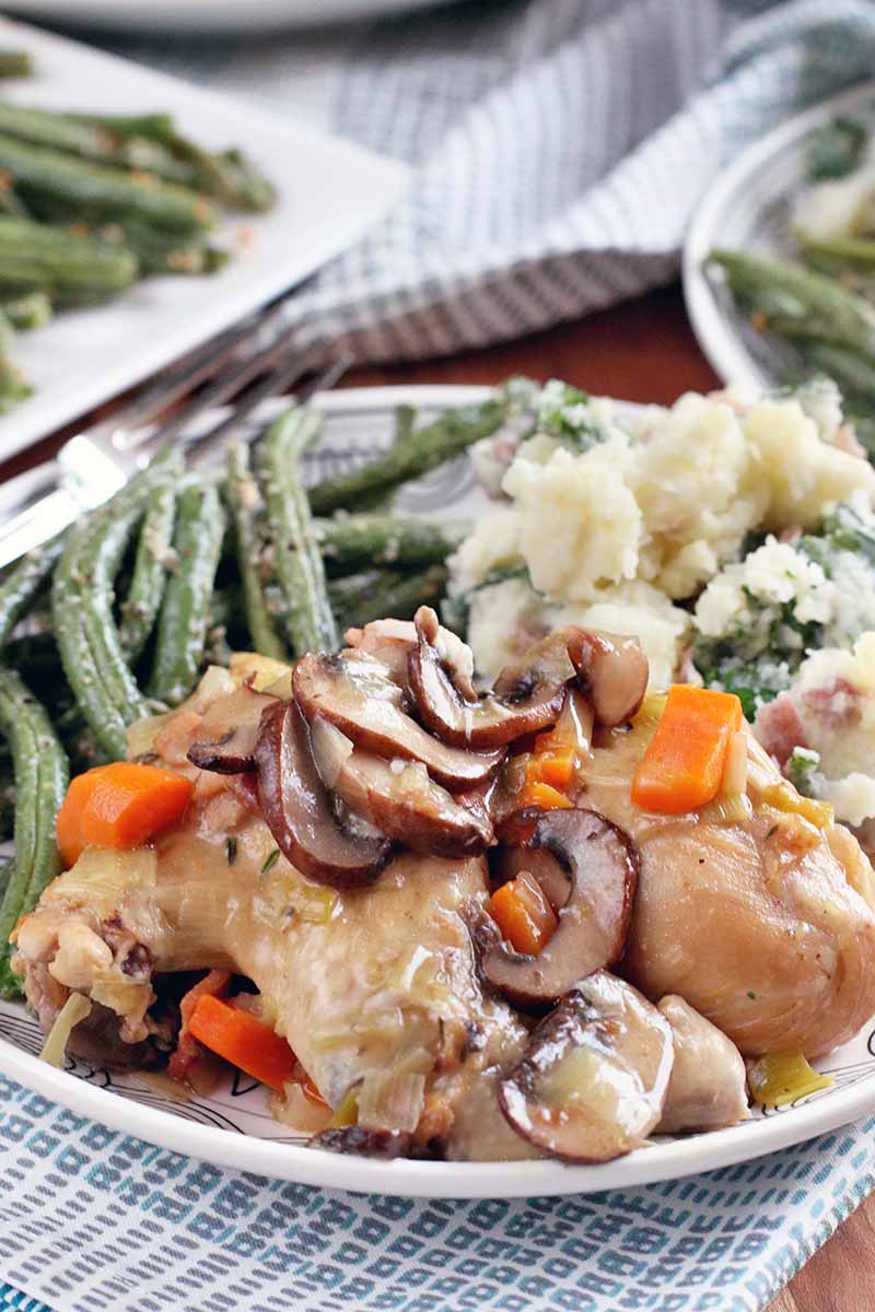 Vertical closely cropped image of a plate of Coq au Vin Blanc, green beans, and mashed potatoes.