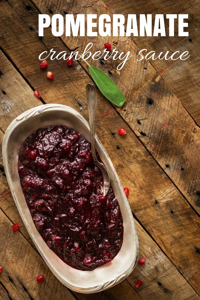 Top-down view of a homemade pomegranate cranberry sauce in a white, porcelain, oblong serving dish on a rustic wooden surface.