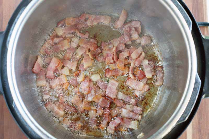 Fat is being rendered out of bacon in the bottom of a metal pressure cooker insert.