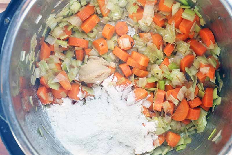 Sauteed carrots and leeks in the bottom of a metal pressure cooker insert.
