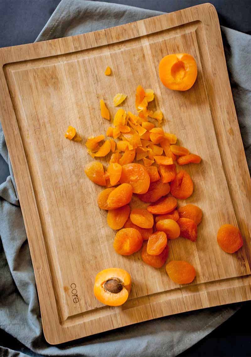 Overhead vertical shot of whole fresh and dried apricots on a wood cutting board, on top of a wrinkled gray cloth.
