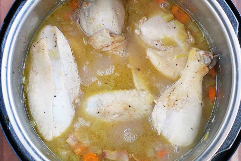 Chicken, a yellow liquid, and chopped vegetables are in the bottom of an Instant Pot.
