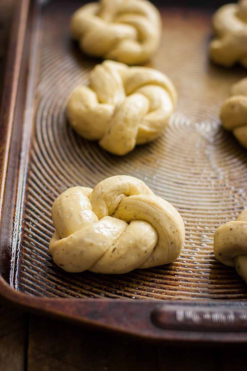 Unproofed dinner roll dough tied into knots sitting on a baking sheet. Closeup view.