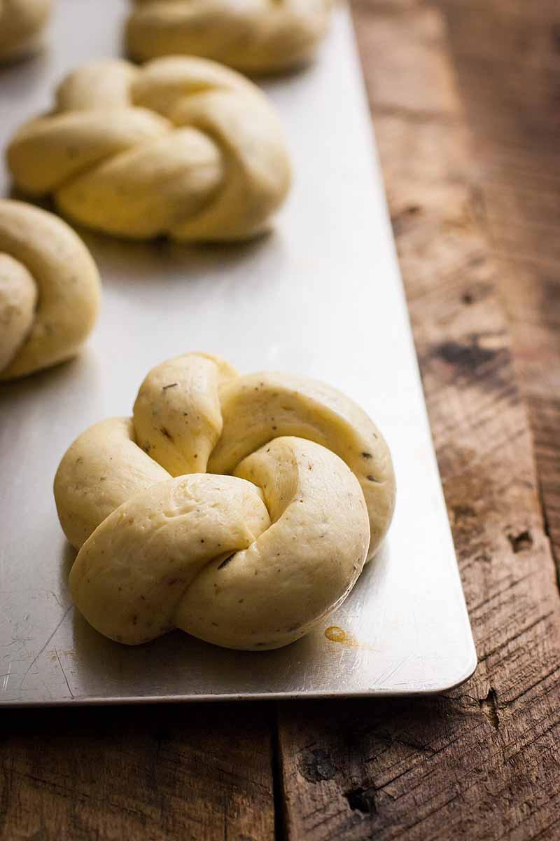 Closeup shot of knotted vegan-friendly dinner rolls sitting on a silver baking pan after proofing put prior to baking.