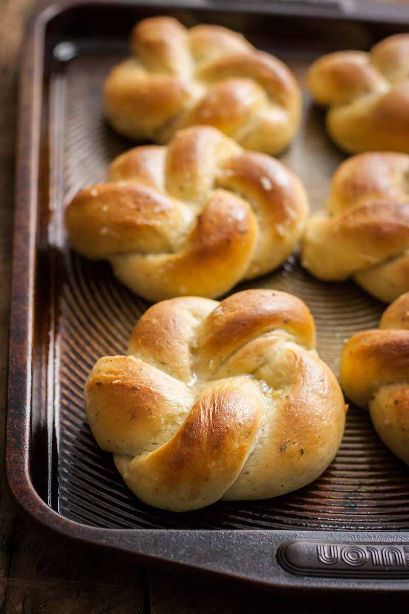 Closeup shot of a batch of dinner rolls on a baking sheet with shallow depth of field and selective focus on the front roll with others being out of focus.