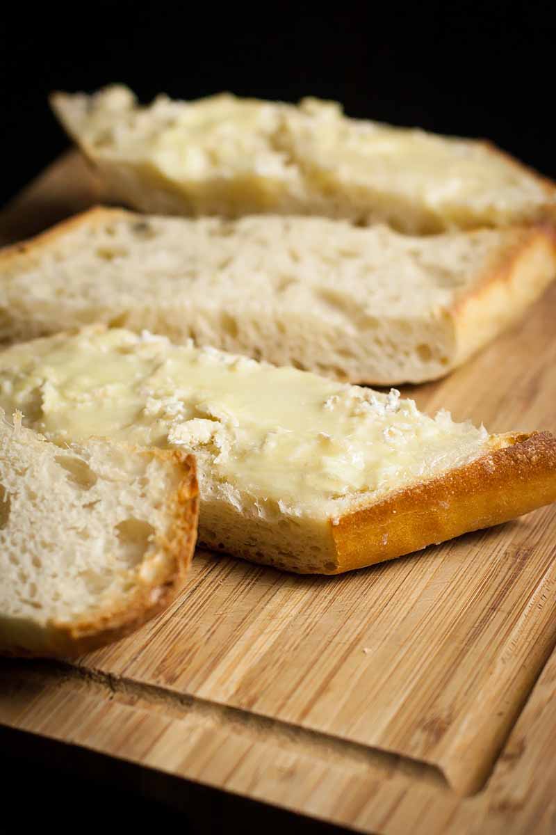 Vertical image of ciabatta spread with cheese on a wooden cutting board.