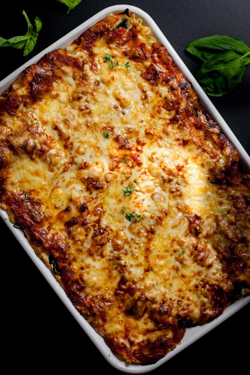 Top down view of a entire cheesy vegetarian lasagna in a white casserole dish on a black background.