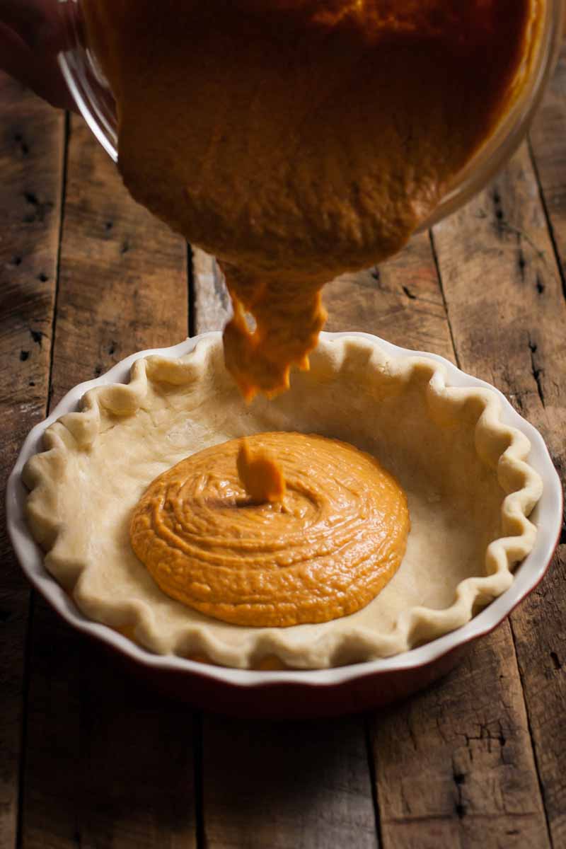 A vegan pumpkin puree mixture is being poured into a prepared pastry crust to make a Thanksgiving dessert.