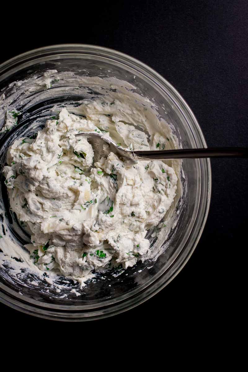 Top down view of creamy ricotta and herb filling in a glass mixing bowl.