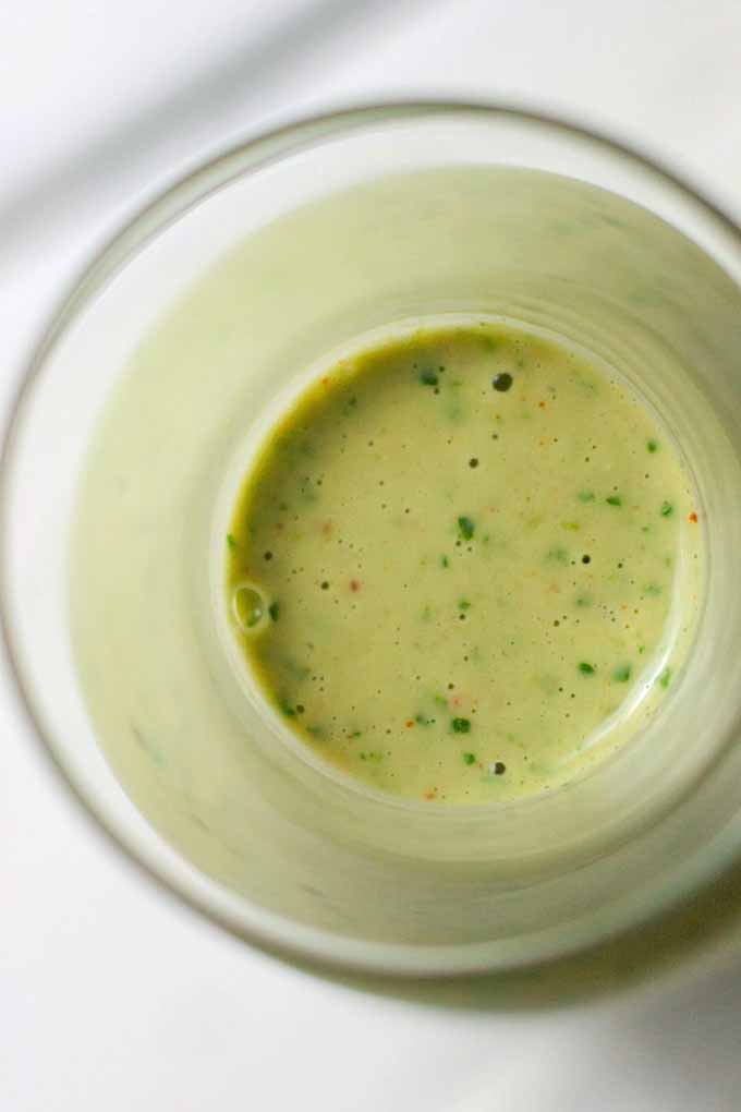 Top-down image of a glass bottle with a pale green cilantro and tahini sauce at the bottom, on a white background.