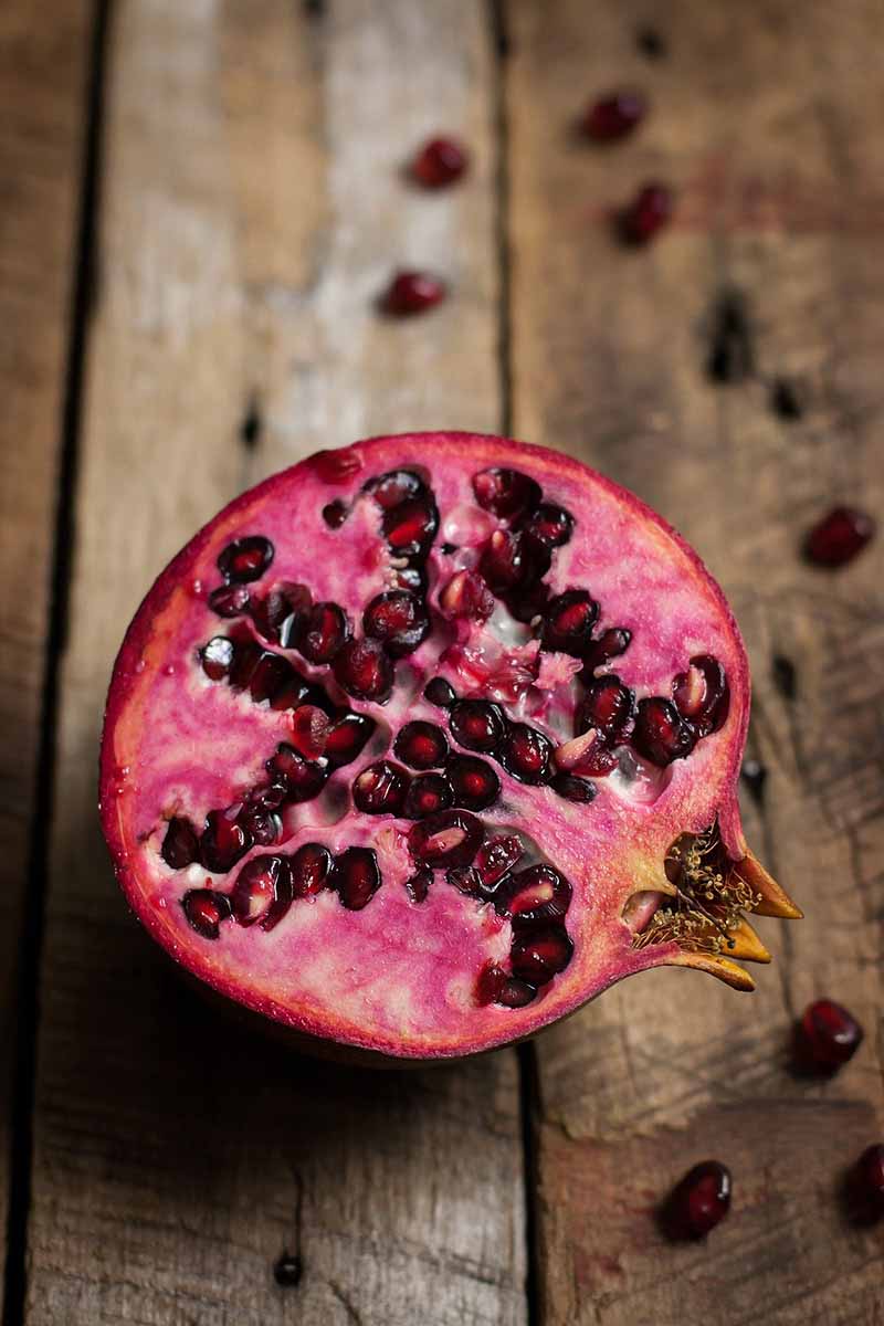 Close up of pomegranate that has been sliced in a half. The fruit is sitting on weathered wooden surface. 