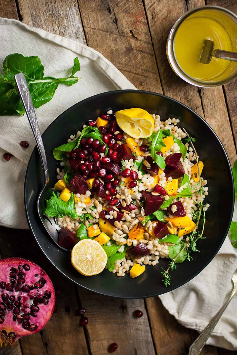 Top down view of a salad composed of butternut squash, arugula greens, beets, pomegranate seeds, and a lemon dressing.