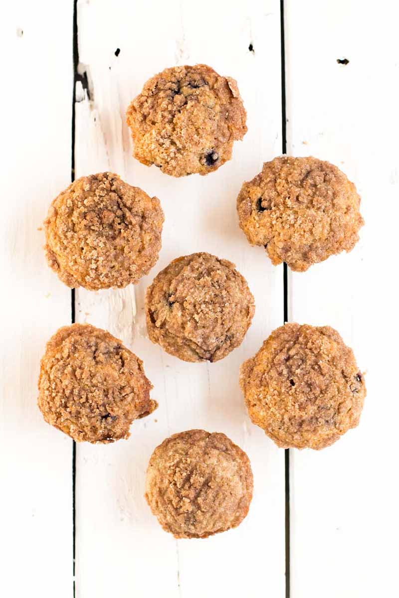 Vertical overhead shot of seven muffins arranged in a hexagonal pattern on a white painted wood surface.