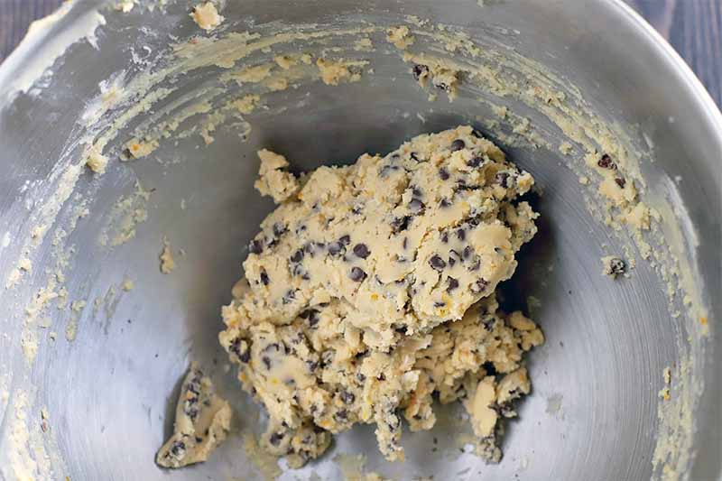 A large stainless steel mixing bowl of chocolate chip cookie dough.