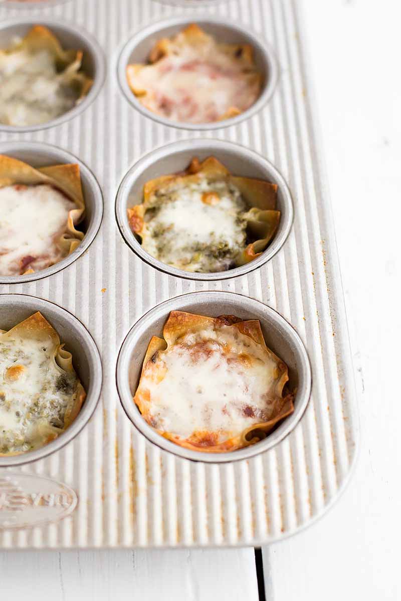 Vertical image of baked lasagna cups in a muffin tin.