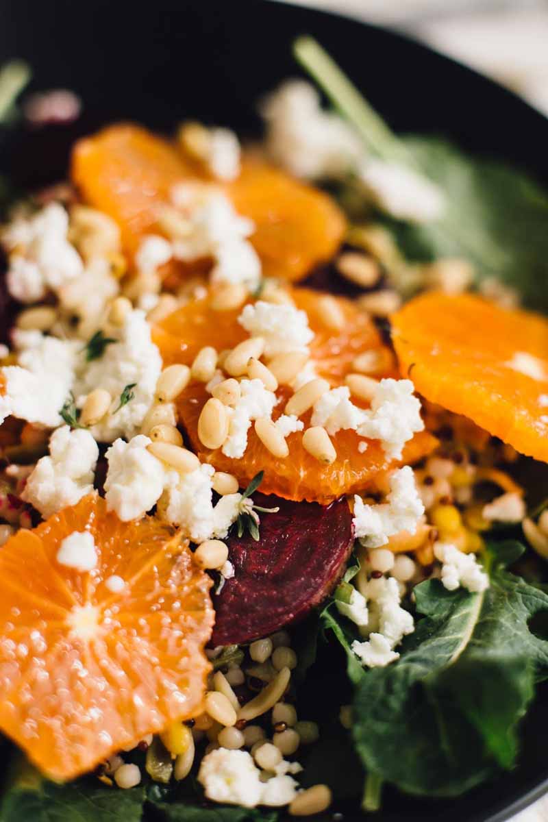 A close up of a Orange and Beet salad made with cooked beets, oranges, baby spinach, goat cheese, pine nuts, and couscous