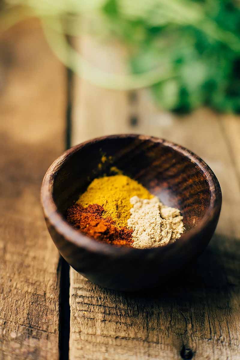 Vertical image of a bowl of spices and herbs in the background on a wooden surface.