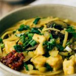Horizontal image of a bowl of tofu and mushroom curry with fresh garnishes