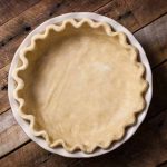 Horizontal image and top down view of a vegan pie crust in a pan sitting a rustic, dark, wooden table.