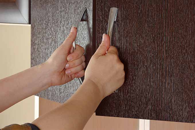 Closeup of two hands grasping cupboard handles to open the doors.