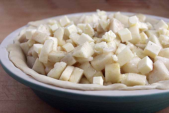 A close up of spiced, raw apple and pear chunks sitting in an unbaked pie crust.