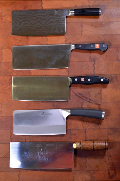 Top view of 5 Chinese Chefs Knifes/Veggie Cleavers on a dark wooden cutting board.