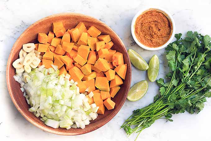 Diced and chopped vegetables, squash, and cilantro along with a a bowl of spices for the pumpkin curry.