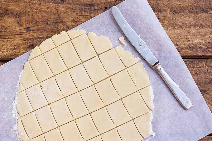A butter knife being used to cut the dough into rectangles to make the cracker shape.