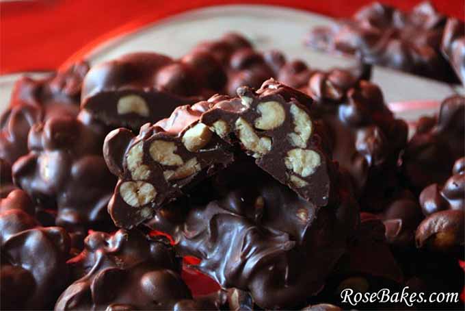 Closeup horizontal image of dark chocolate peanut clusters, with the one in the front sliced in half to show the nuts inside, blurring to soft focus with a red background.