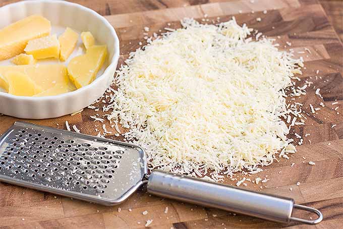 Shredded Parmesan cheese on a wooden cutting board.