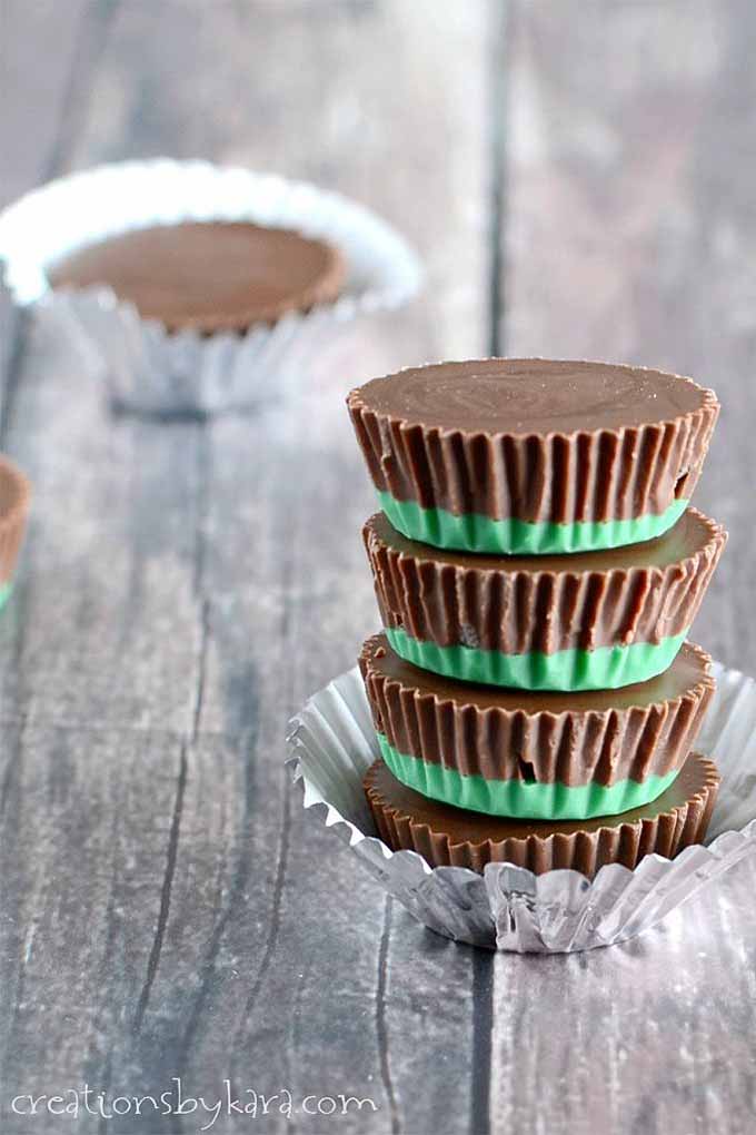 Vertical image of a stack of four green and brown chocolate and mint candy cups in a silver paper wrapper, with a few more in the background, on an unfinished weathered wood surface.