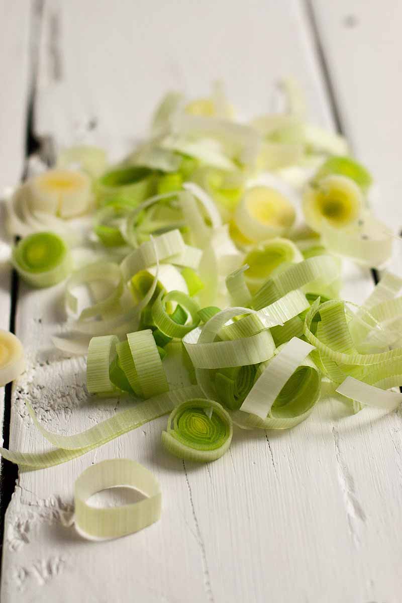 Close up of a small batch of sliced leeks on a white, wooden table.