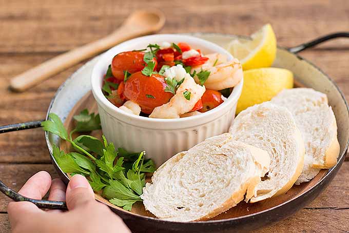 Roasted tomatoes with feta cheese and shrimp, accompanied by fresh bread and lemon wedges.