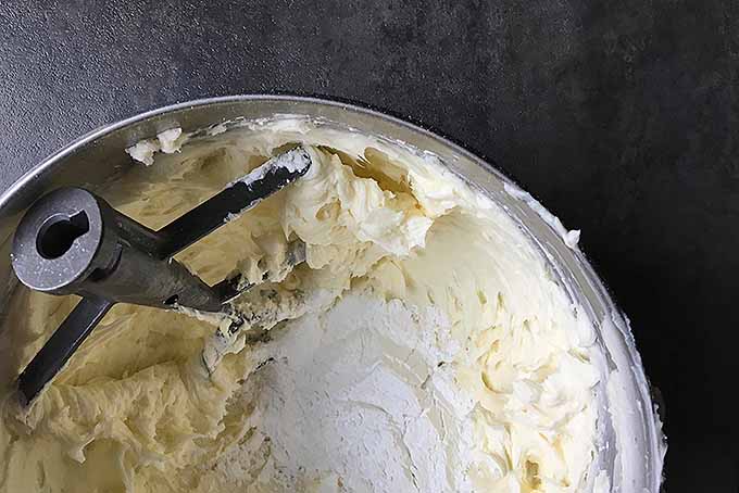 Adding powdered sugar to a bowl of whipped butter for American-style vanilla buttercream frosting | Foodal.com