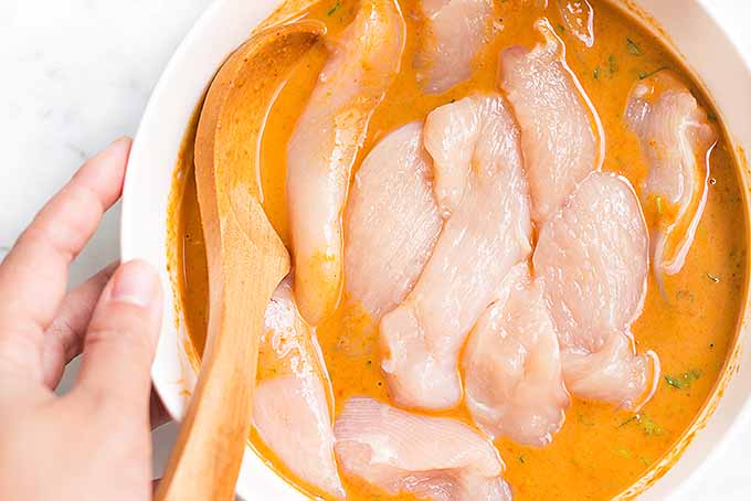 Marinating chicken strips in a coconut curry sauce for our spicy satay recipe. | Foodal.com