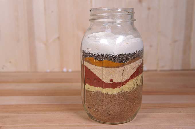 A mason jar filled with coloful powdered spices in layers.