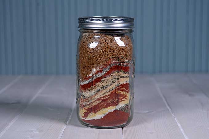 A mason jar filled with layered spices for a mixture used to make a superb all-purpose chicken dry rub. | Foodal