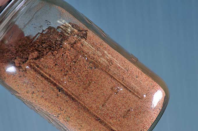 Close up of a mason jar containing the ingredients for an all-purpose chicken dry rub recipe. The jar is being shaken to mix the spices | Foodal