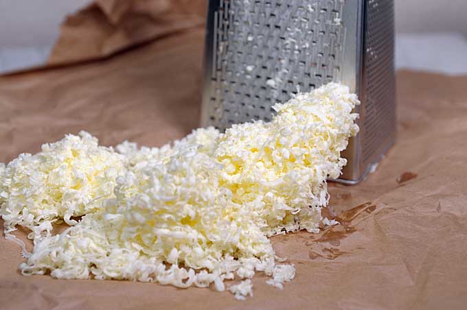 Cold chilled butter being shredded using a box grater.