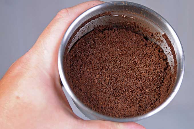 A close up of a stainless container from a blade grinder showing ground coffee beans.
