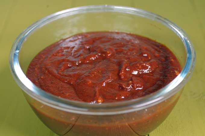 Close up of a glass bowl full of apple cider bbq sauce on a light green background.
