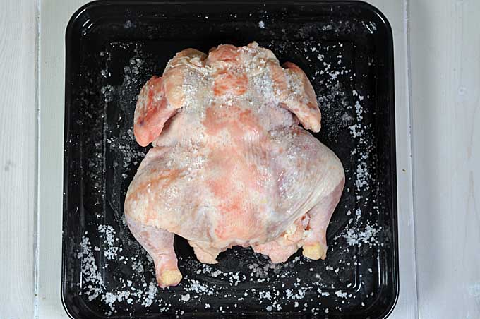 Top down view of chicken in a black pan that has been brined with coarse salt and allowed to chill in a refrigerator for 24 hours | Foodal