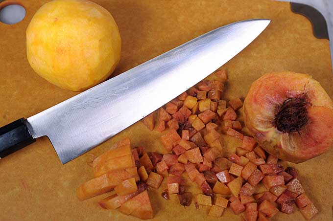 A Japanese gyuto kitchen knife being used to dice up peaches.