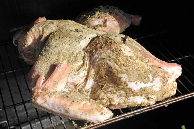 A brined and dry rubbed turkey carcass sitting on a smoker rack in a propane Camp Chef Smoke Vault | Foodal
