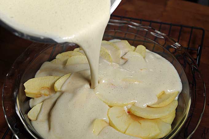 Egg dough being poured over apple slices | Foodal