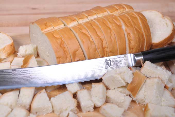 A loaf of Italian bread being made into bread chunks. A Shun bread knife is in the foreground.