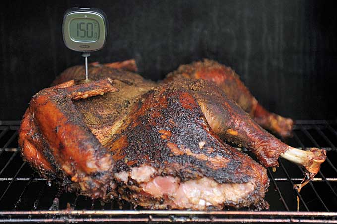 A fully smoke turkey with a meat thermometer sticking out of it showing 150 degrees F | Foodal