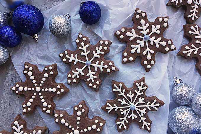 Snowflake-shaped chocolate brownie cut-out cookies, with blue and silver Christmas baubles on crumpled white parchment paper.