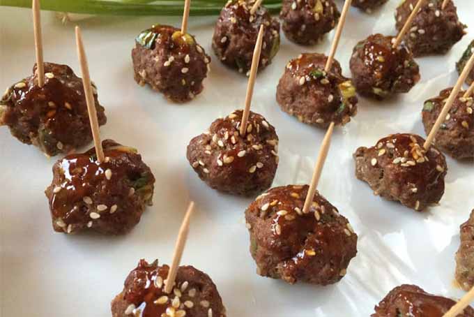 Teriyaki meatballs arranged in rows on a plate and skewered with toothpicks for easy serving.